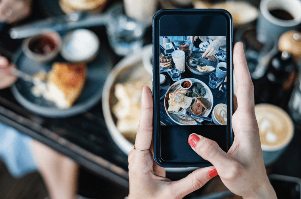woman's hands holding smart phone taking photo of food on restaurant table