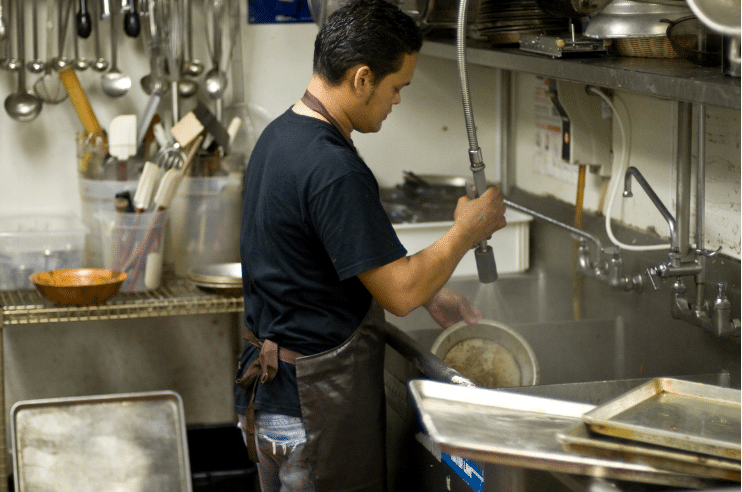 Man rinsing pan in a commercial dishwasher